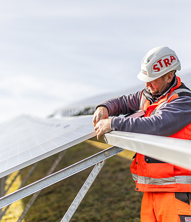 Mit dem Aufbau von Photovoltaik-Anlagen durch STRABAG werden die ESG-Ziele umgesetzt. Foto eines STRABAG Bauarbeiters der dabei ist eine Photovoltaik-Anlage aufzubauen.