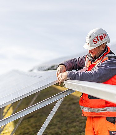 Mit dem Aufbau von Photovoltaik-Anlagen durch STRABAG werden die ESG-Ziele umgesetzt. Foto eines STRABAG Bauarbeiters der dabei ist eine Photovoltaik-Anlage aufzubauen.