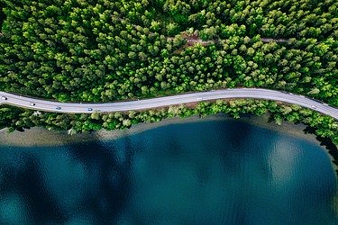 Foto einer Straße, die neben einem See und einem Wald verläuft
