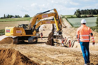 A STRABAG employee walks towards an excavator that is laying cables
